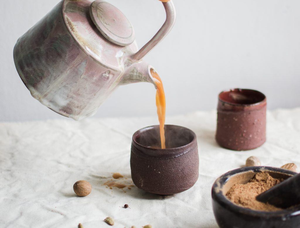 Tea is poured from a silver tea kettle into a clay mug.