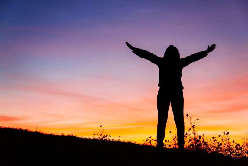 A woman stretches her arms out facing the dawn.