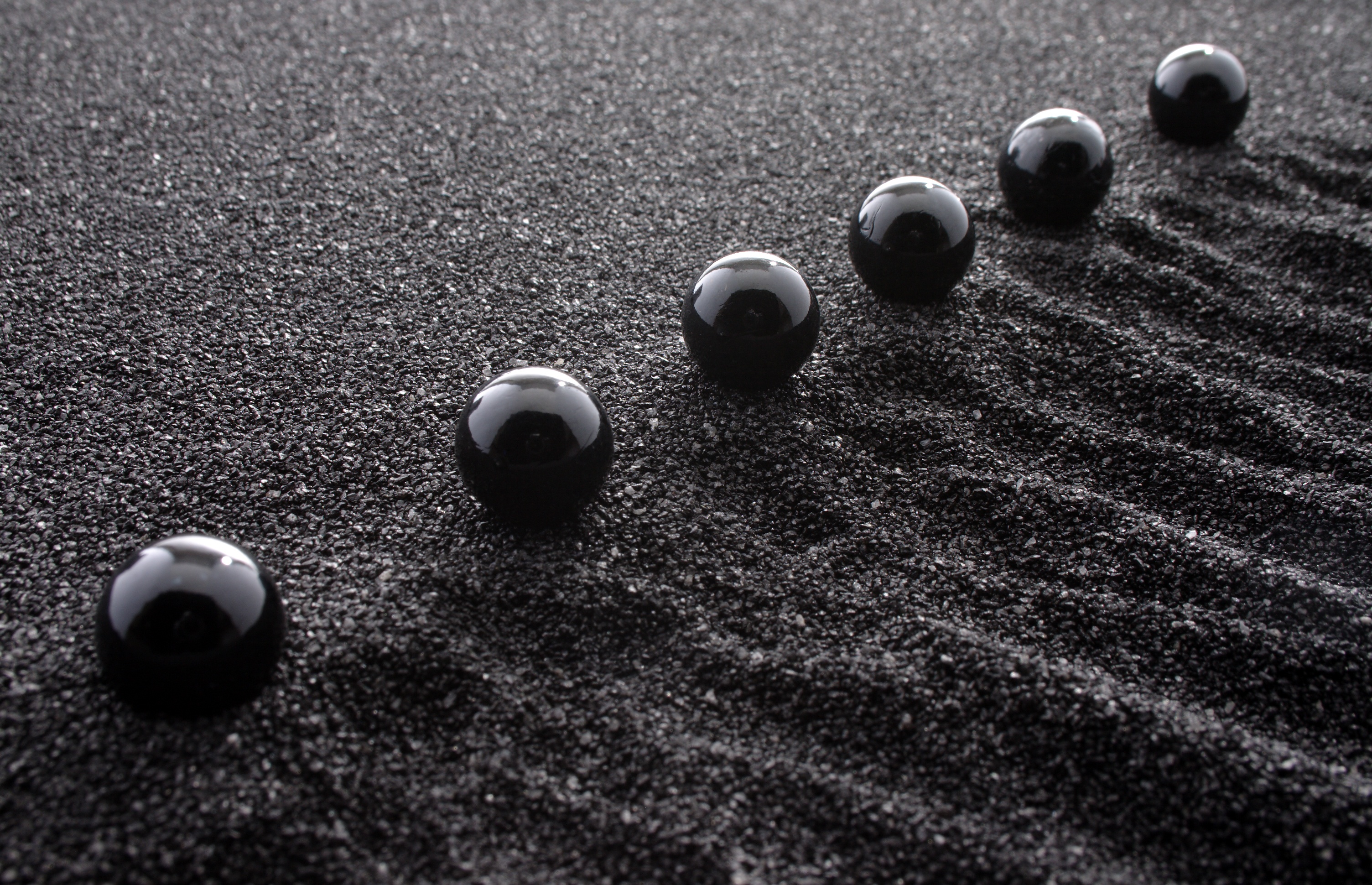 Black marbles in a straight line on sand