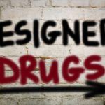 The words "Designer Drug" written in spray paint on a white wall with an arrow point rights