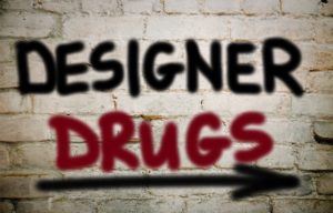 The words "Designer Drug" written in spray paint on a white wall with an arrow point rights